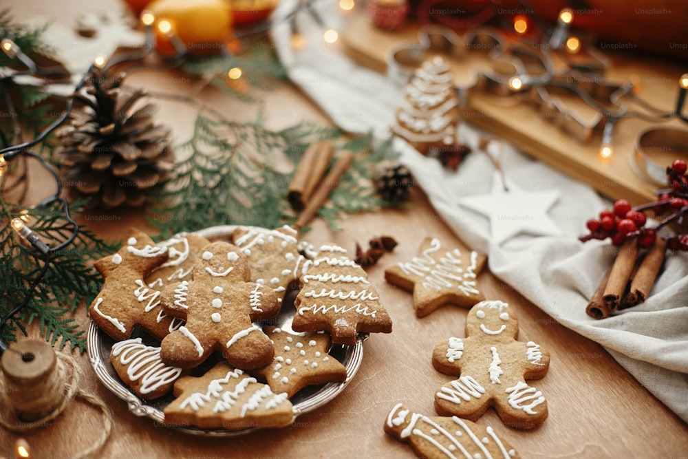 Christmas gingerbread cookies on vintage plate and anise, cinnamon, pine cones, cedar branches  with golden lights on rustic table. Baked traditional gingerbread man, tree, star cookies
