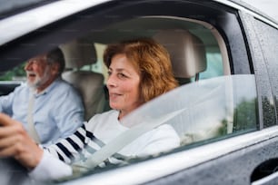 Una feliz pareja de ancianos sentados en el coche, conduciendo y hablando.