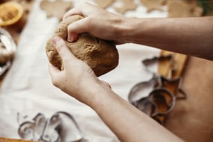 Making christmas gingerbread cookies. Hands kneading raw dough on background of rolling pin,metal cutters, anise, ginger, cinnamon, pine cones, fir branches on rustic table.