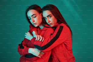 Trying new red jackets. Studio shot indoors with neon light. Photo of two beautiful twins.