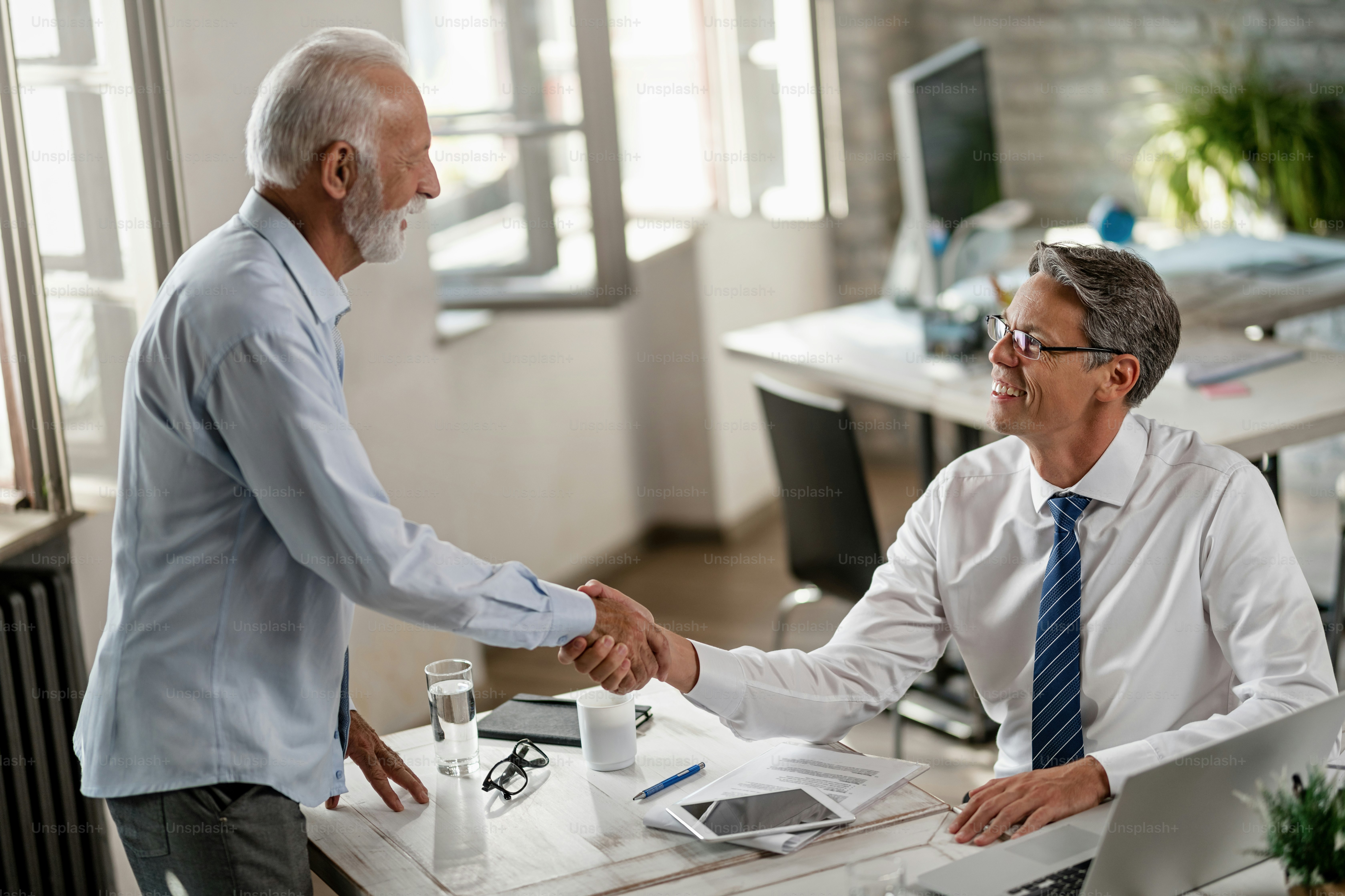 Happy bank manager shaking hands with senior man while meeting in the office.