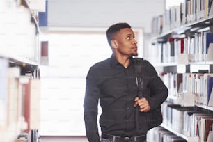 Going forward with backpack. African american man in the library searching for some books.