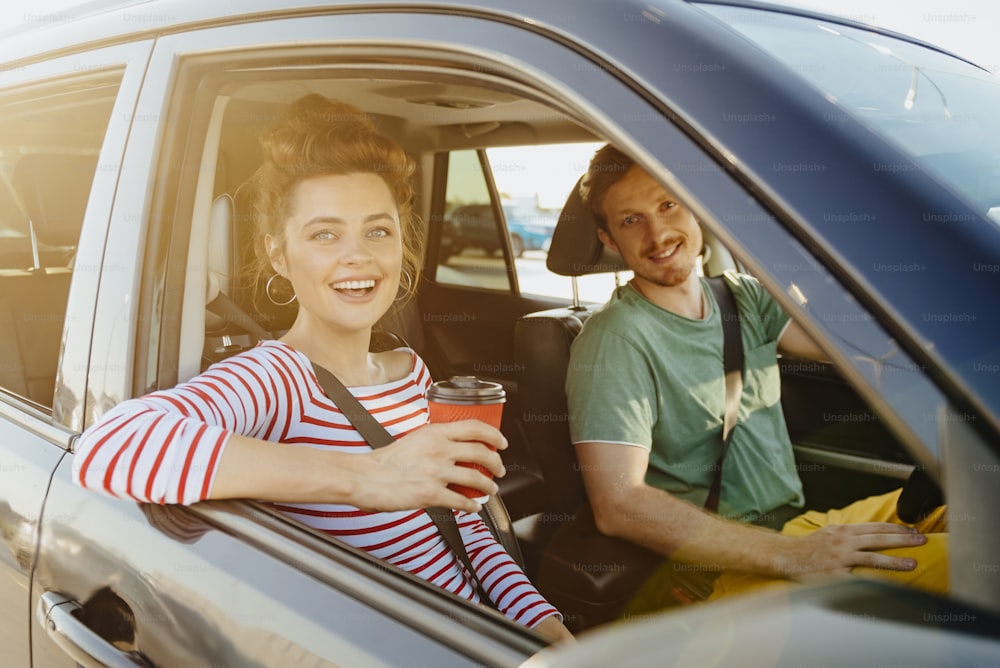 Happy young couple is travelling together by car with hot drinks