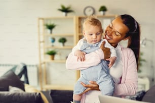 Happy mother enjoying while holding her baby son and spending time with him at home.