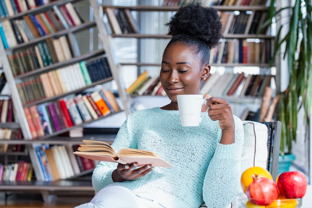 Cozy sofa and a beautiful girl, reading a book, concepts of home and comfort, place for text. Young pretty woman sitting and drinking coffee wile reading a book enjoys of rest