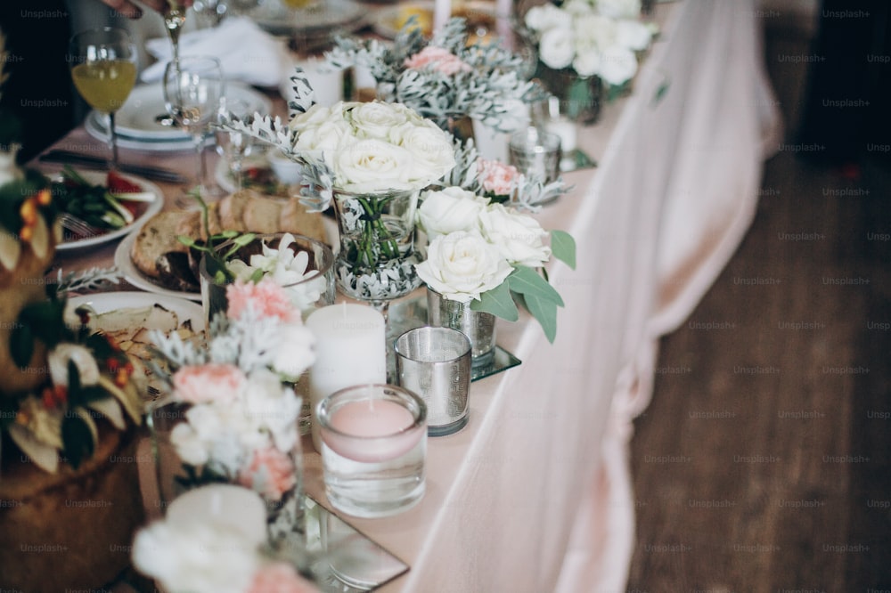 Candle, White  flowers in modern glass vase on pink centerpiece. Stylish luxury decor on wedding table.Luxury catering and adorning. Holiday feast