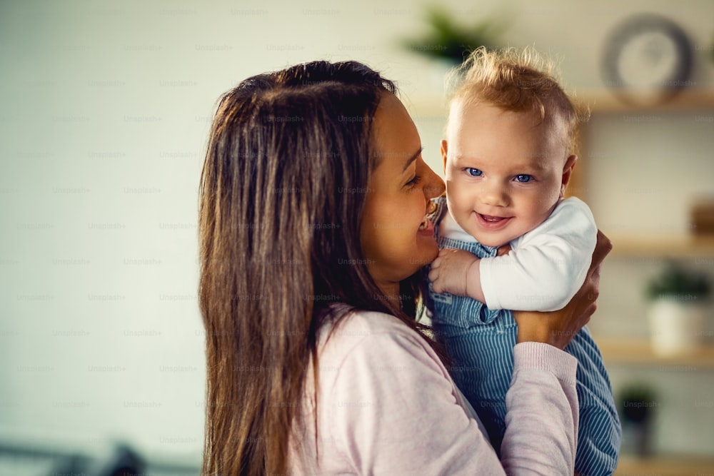 Happy baby boy having fun with his mother at home and looking at camera.