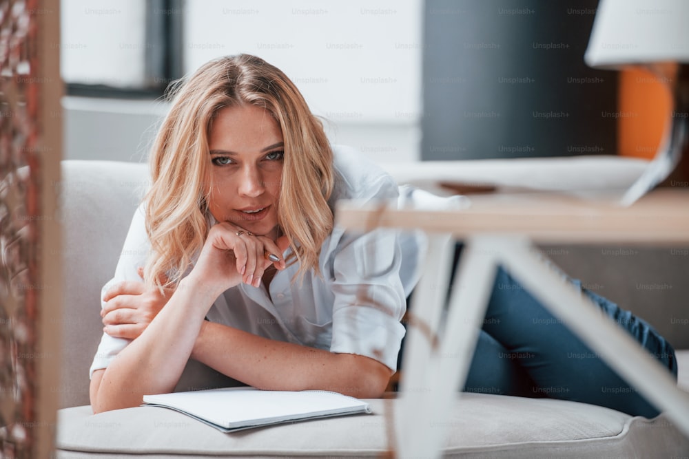 Lying down on sofa. Businesswoman with curly blonde hair sitting in room against window.