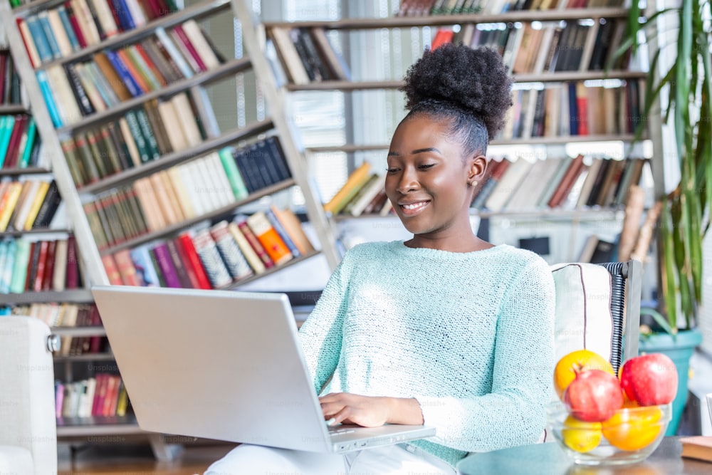 Young woman doing research work for her business. Smiling woman sitting on sofa relaxing while browsing online shopping website. Happy girl browsing through the internet during free time at home.