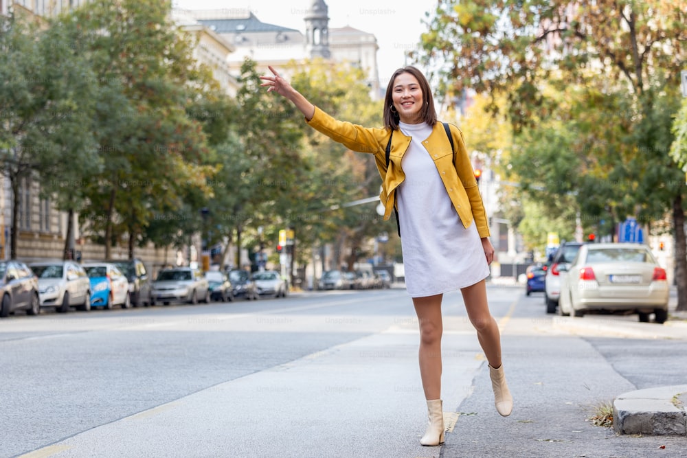 Young woman hailing a taxi ride. Beautiful charming woman hailing a taxi cab in the street. Businesswoman trying to hail a cab in the city. Tourist woman hailing a taxi