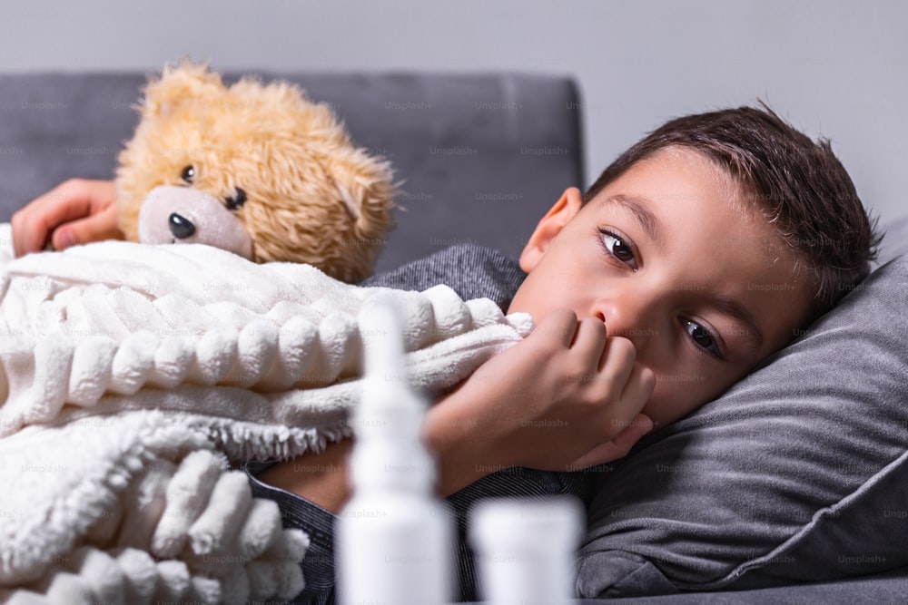 Sickness, seasonal virus problem concept. Boy being sick having flu lying on sofa looking at temperature on thermometer. Sick Kid lying in bed with high fever. Cold flu and migraine.