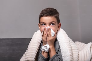 Cold And Flu. Portrait Of Ill boy Caught Cold, Feeling Sick And Sneezing In Paper Wipe. Closeup Of Young Unhealthy kid Covered In Blanket Wiping Nose. Healthcare Concept.