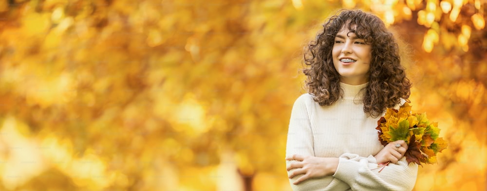 Young woman with autumn bouquet of maple leaves. Girl with a dental braces and curly hair.