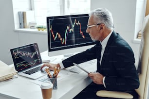 Senior trader in elegant business suit using computer while working at the office