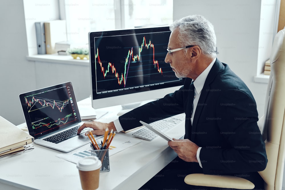 Senior trader in elegant business suit using computer while working at the office