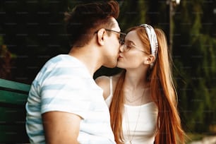 Side view portrait of a lovely young couple kissing while sitting on a bench outside while traveling.