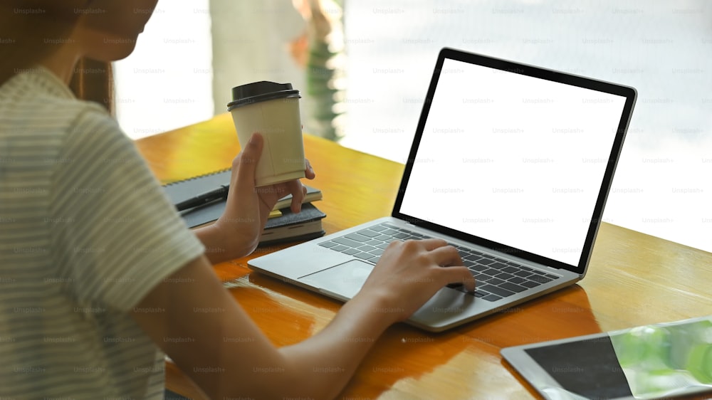 Female's using her laptop with empty screen and holding coffee cup.