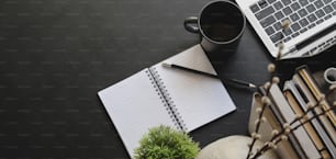 Overhead shot of dark modern workplace with laptop computer and office supplies on black table background