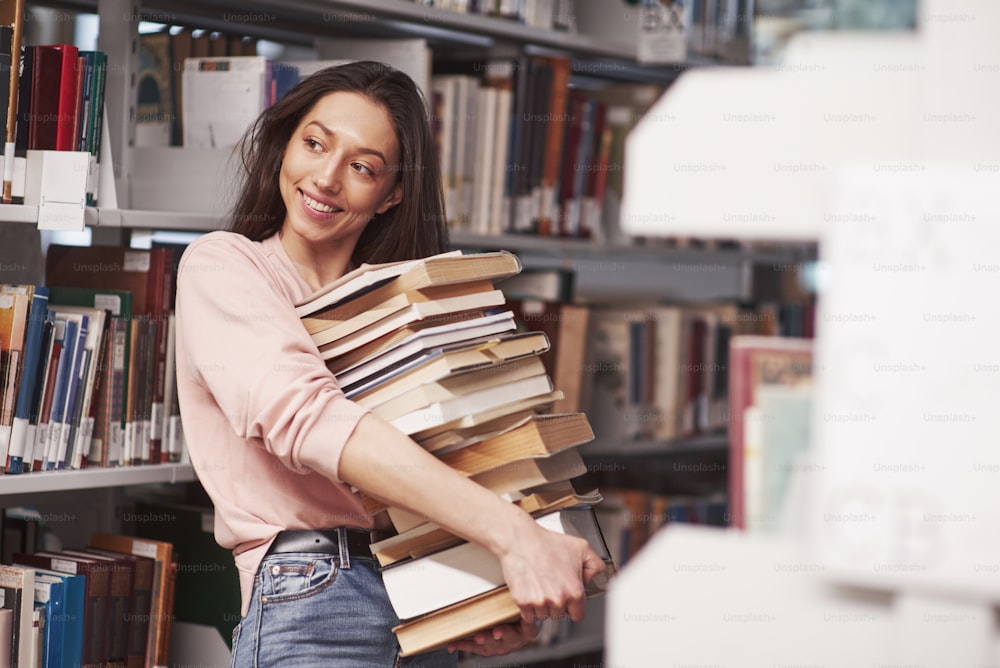 More than enough. Brunette girl in casual clothes having good time in the library full of books.