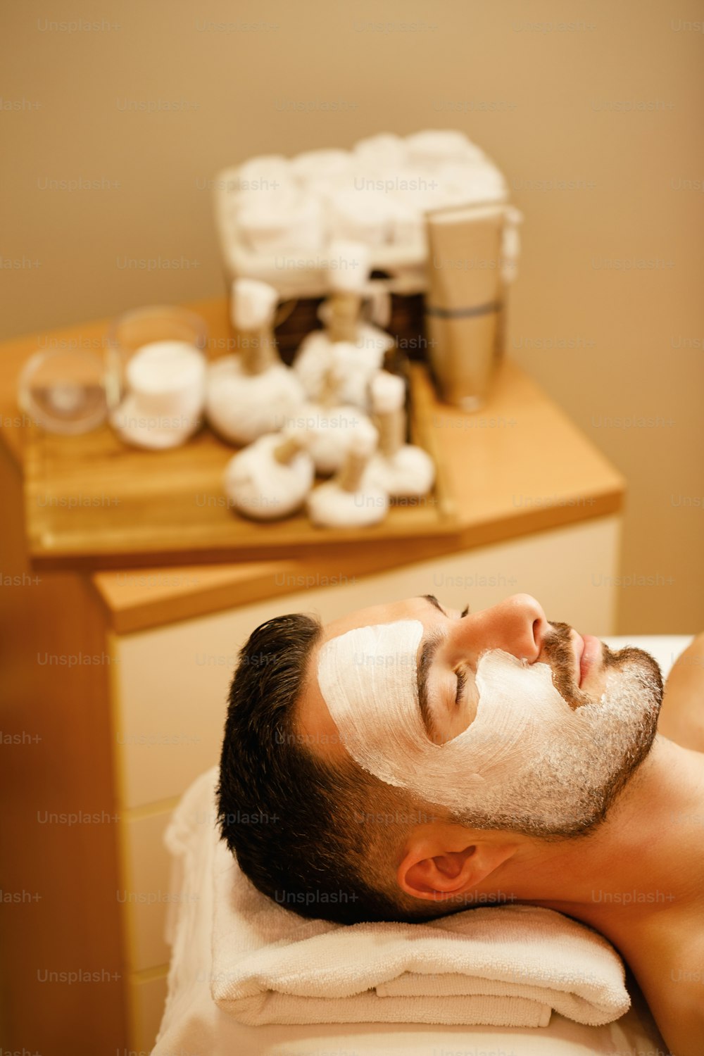 Giovane uomo con maschera facciale nutriente che si rilassa durante il trattamento cosmetico alle terme.