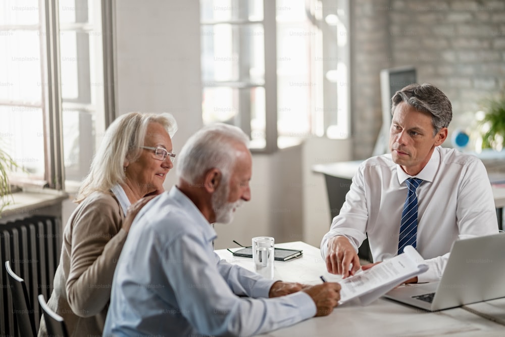 Senior couple signing a contract while being on a meeting with bank manager. Focus is on manager.