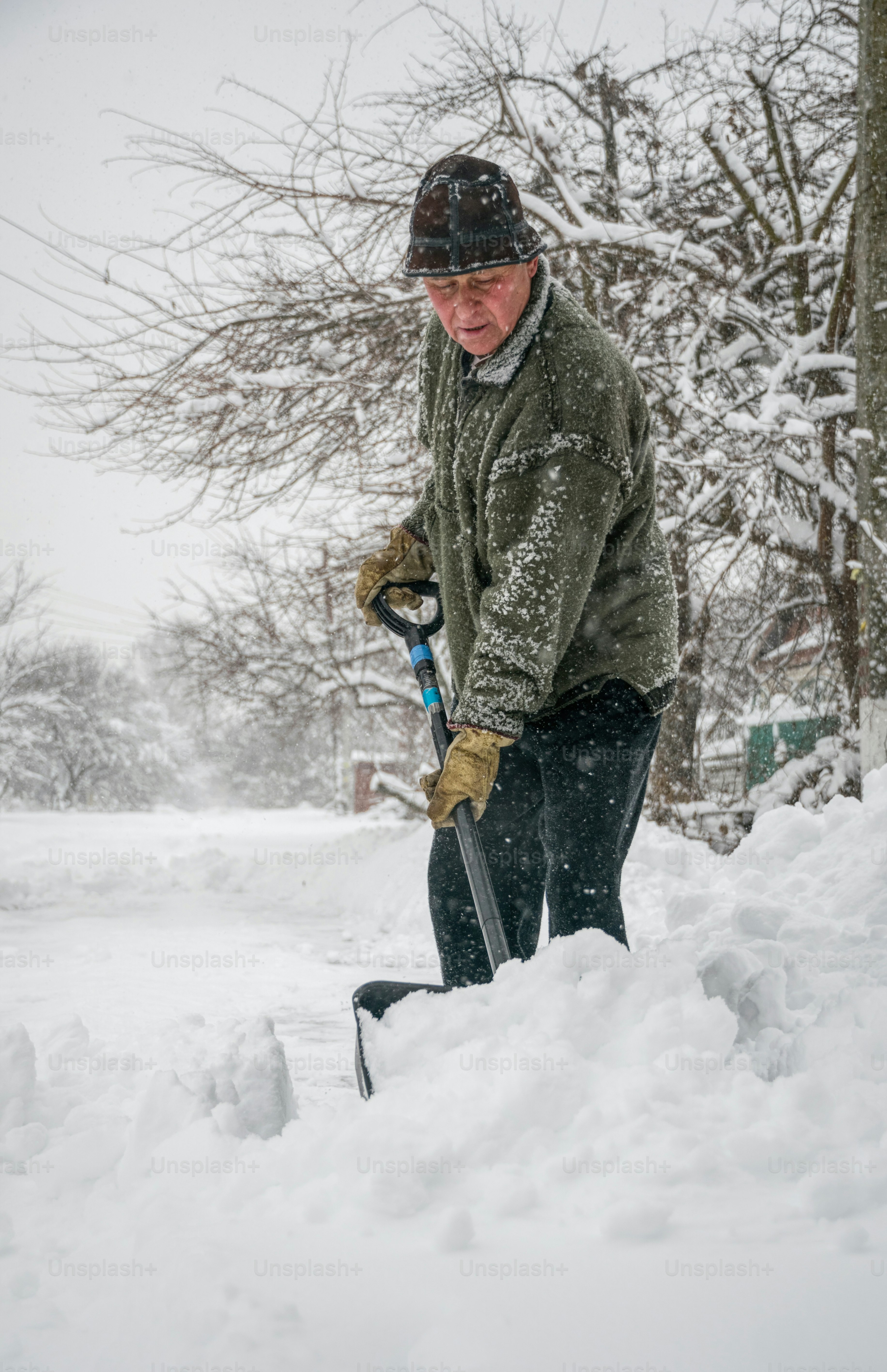 Winter snow removal. A man with a shovel clears the yard and driveway from snow during heavy snow