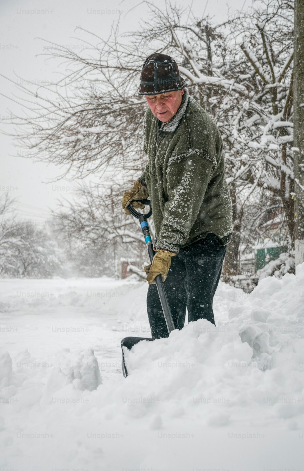 Remoção de neve de inverno. Um homem com uma pá limpa o quintal e a garagem da neve durante a neve pesada