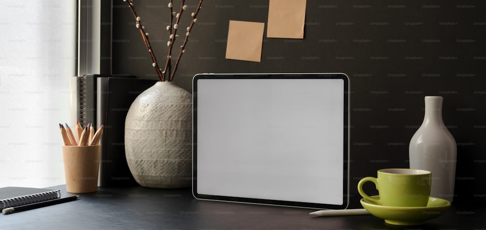 Trendiger Büroraum mit leerem Bildschirm digitales Tablet mit Bürobedarf und Dekorationen