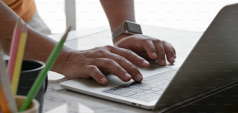 Foto recortada de un hombre de negocios escribiendo en una computadora portátil mientras trabaja en su proyecto en un lugar de trabajo cómodo