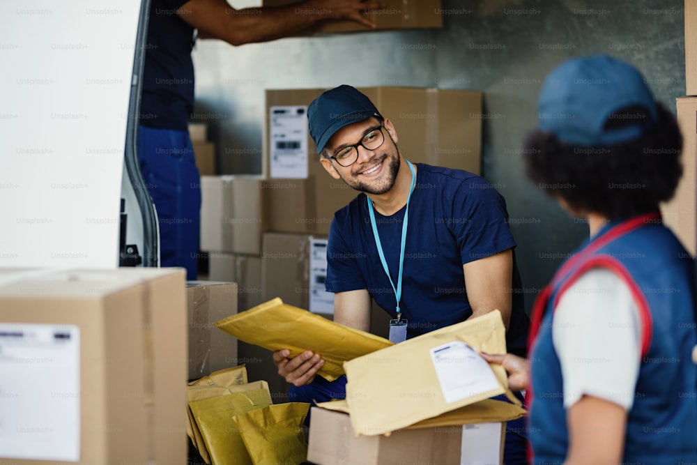 Young manual worker talking to his female colleague while sorting packages for shipment in a delivery van.