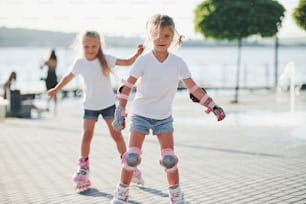Two cute kids riding by roller skates in the park at daytime.