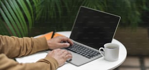 Giovane sparato ritagliato che lavora al suo progetto con computer portatile e forniture per ufficio sul tavolo bianco in giardino