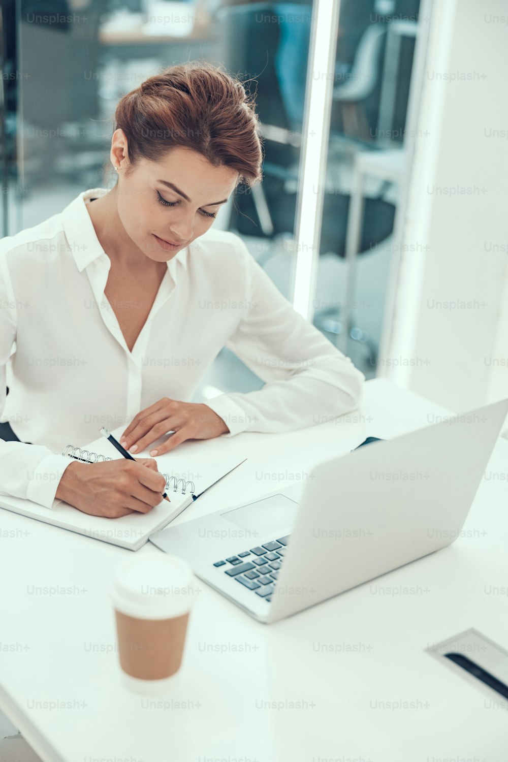 Mujer joven ocupada sentada en su lugar de trabajo en la oficina y tomando notas