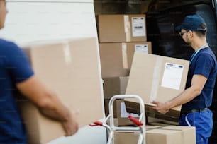 Delivery man carrying cardboard boxes and loading them in a mini van.