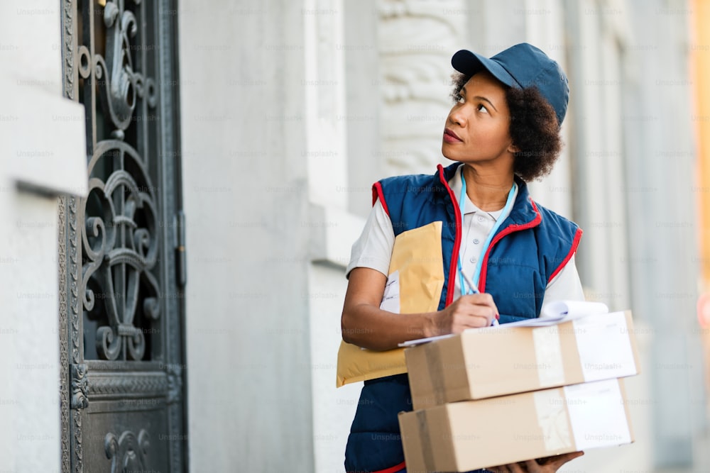 African American female deliverer writing notes while dispatching packages in the city.