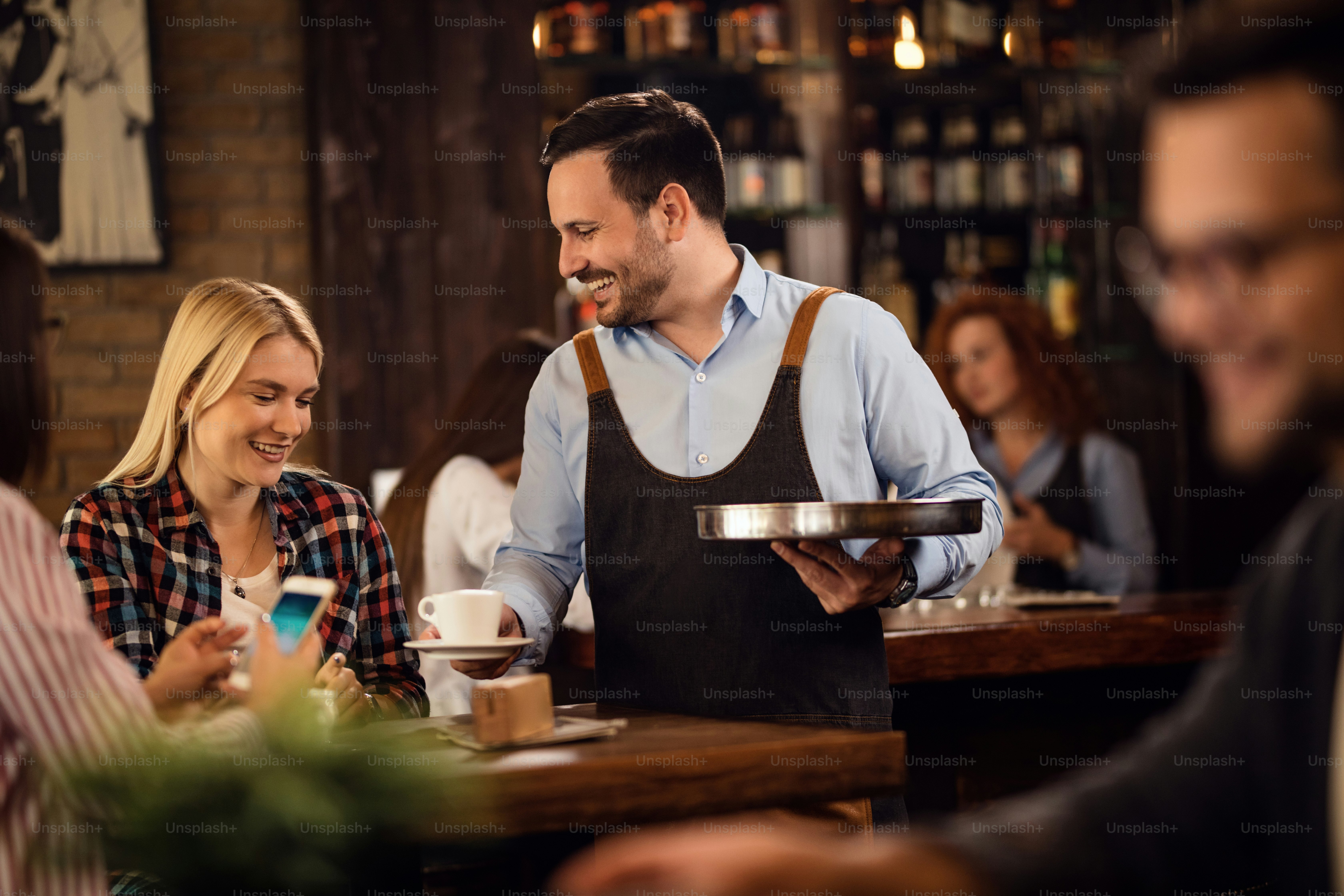Young happy woman enjoying while waiter is serving her coffee in a cafe ...