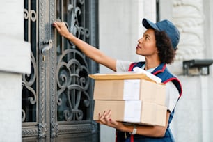 Black female courier knocking on front door while delivering packages.