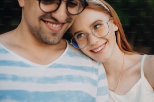 Close up of an attractive young female with red hair and freckles leaning her head on her boyfriends shoulder smiling looking at him outside while dating.