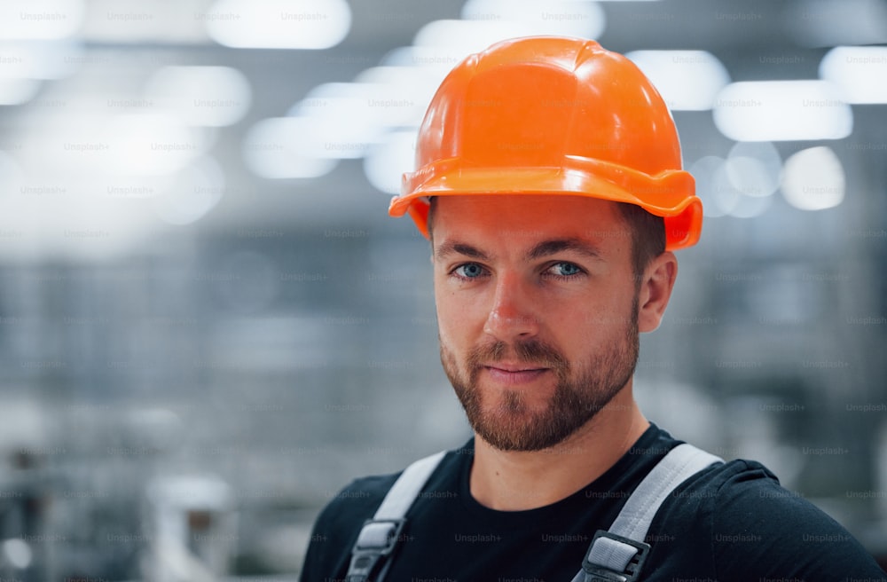 Portrait of male industrial worker indoors in factory. Young technician with orange hard hat.