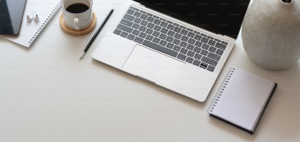 Vue de dessus d’un espace de travail confortable avec ordinateur portable et fournitures de bureau sur une table en bois blanc