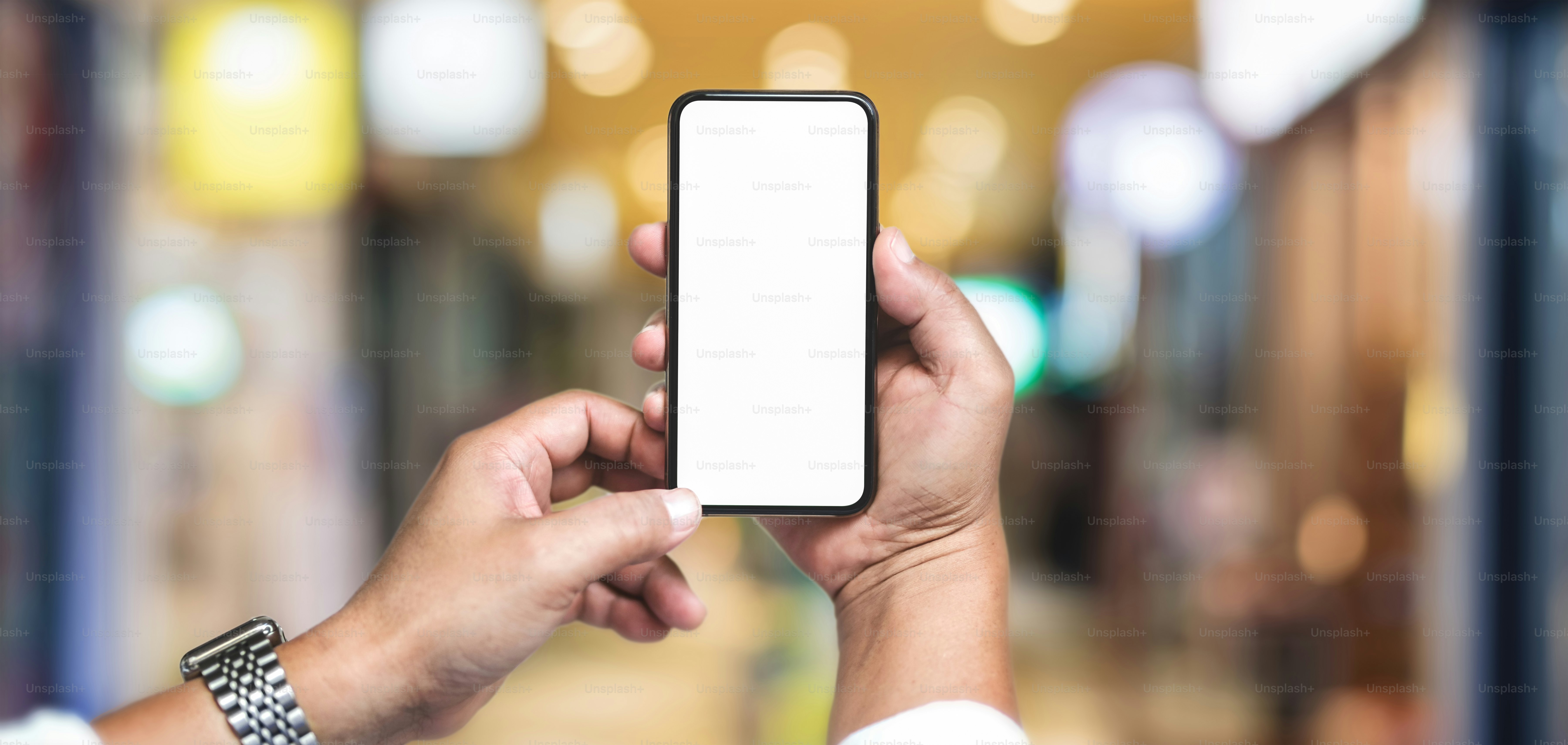 Colpo ritagliato di uomo d'affari che tiene uno smartphone con schermo vuoto con sfondo sfocato dell'ufficio