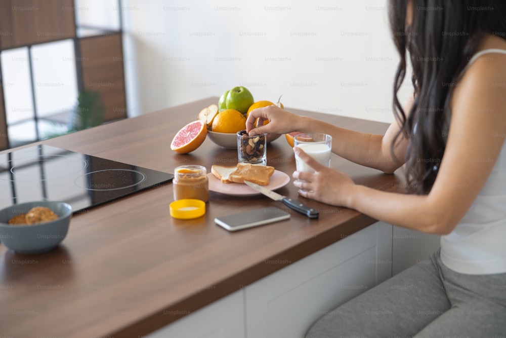 Foto ritagliata di una ragazza che assaggia frutta secca in cucina