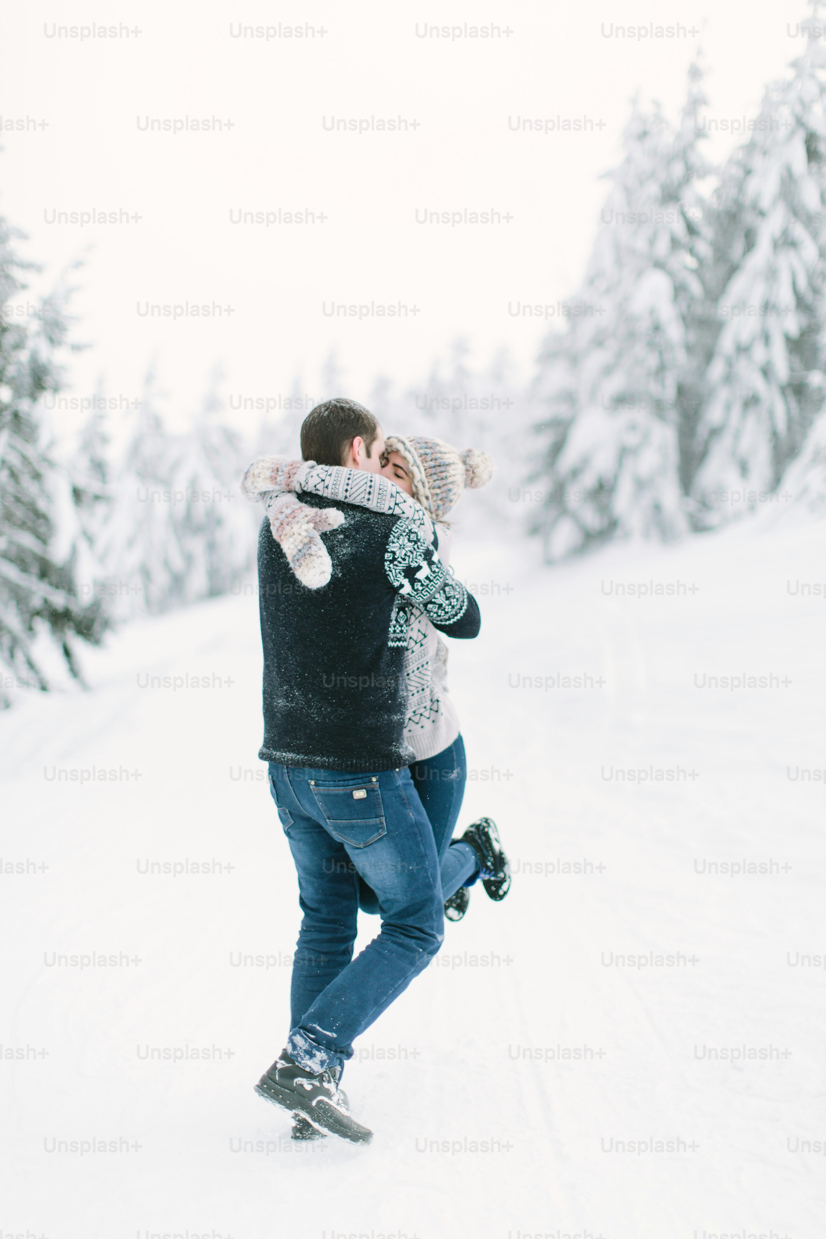 A couple in knitted clothes walks in winter in the forest with trees.