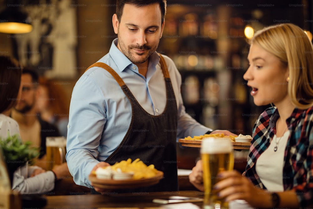 Mid adult waiter giving nachos to a female customer who is drinking beer in a bar.