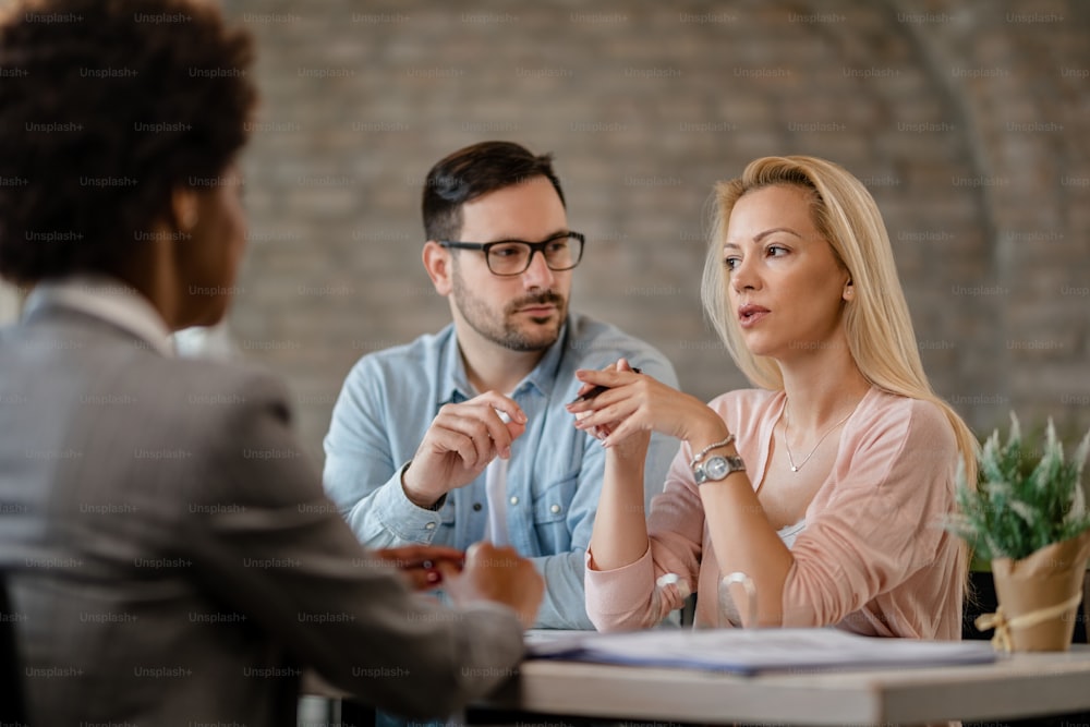 Casal de adultos médios conversando com seu consultor financeiro em uma reunião no escritório. O foco está na mulher pensativa.