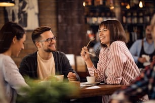 Grupo de amigos felices que se comunican mientras se relajan en una cafetería. La atención se centra en la mujer feliz que sostiene sus gafas.