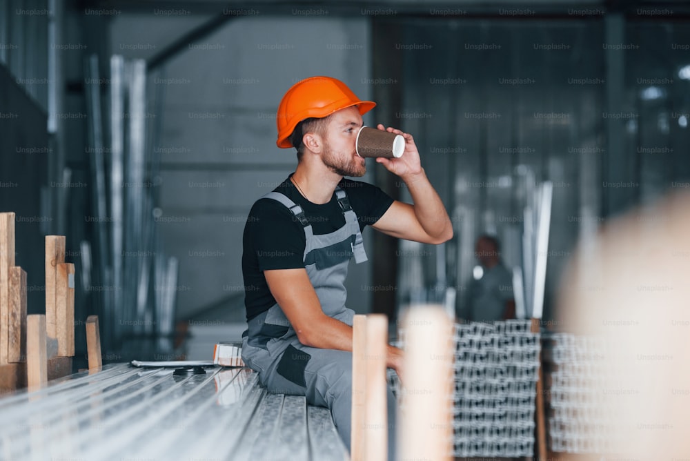 ��음료 한잔과 함께. 점심 시간. 공장 실내의 산업 노동자. 주황색 안전모를 쓴 젊은 기술자.