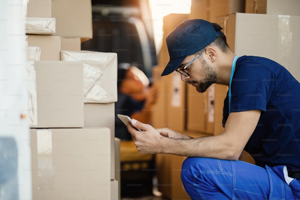 Delivery man working on touchpad while organizing packages for shipment in a van.