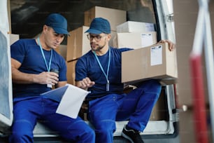 Young couriers going through delivery list while sitting in a van and preparing packages for the shipment.