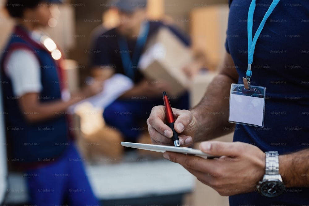 Close-up of manual worker writing with digitized pen on touchpad while preparing for a delivery.